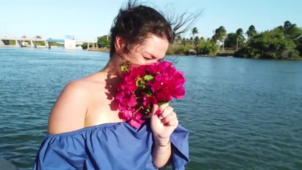 Young attractive brunette woman walks on the background of red spring flowers in park. Girl with red flowers in her hands. — Stock Video