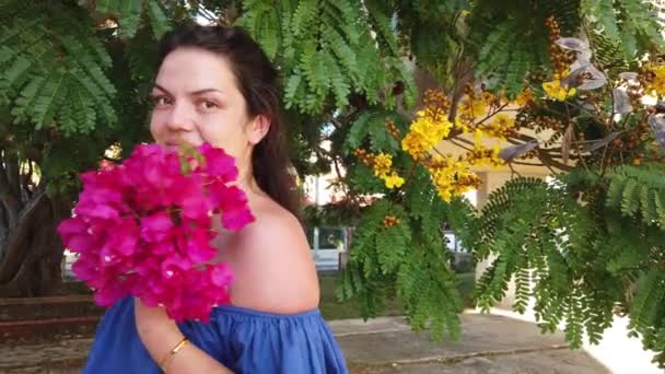Young attractive brunette woman walks on the background of red spring flowers in park. Girl with red flowers in her hands. — Stock Video