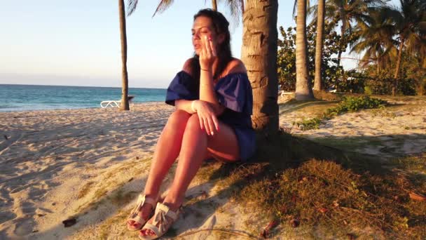 日没時のビーチのヤシの木の上のブルネットの女の子 — ストック動画
