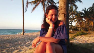 Gün batımında sahilde palmiye ağacının yanında esmer kız