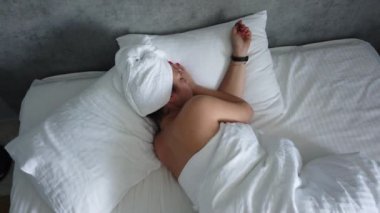 Güzel genç kız beyaz bir yastık üzerinde uyuyor. O uyanma, germe ve gülümseyerek. El gerçek zamanlı orta atış