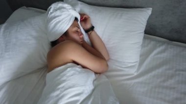 Güzel genç kız beyaz bir yastık üzerinde uyuyor. O uyanma, germe ve gülümseyerek. El gerçek zamanlı orta atış