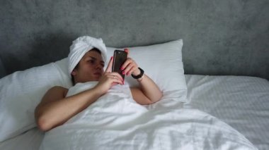 Üst görünümü genç kadın battaniye altında yatakta uyanma. Sevimli kız sabah ilk şey onu akıllı telefon kontrol.