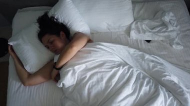 Üst görünümü genç kadın battaniye altında yatakta uyanma. Sevimli kız sabah ilk şey onu akıllı telefon kontrol.