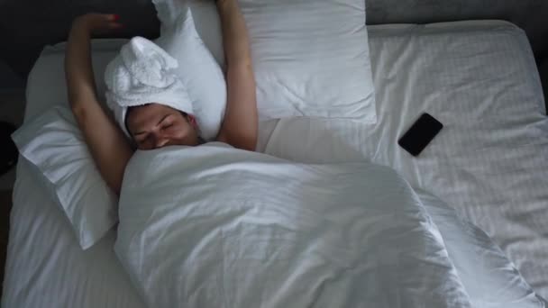 顶视图年轻女性醒来在床上毯子下 可爱的女孩检查她的智能手机在早上的第一件事 — 图库视频影像