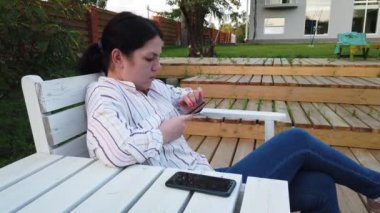 Cep telefonu kadın kullanımı ve bahçesinde evde bankta oturup
