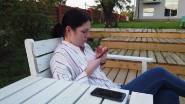Cep telefonu kadın kullanımı ve bahçesinde evde bankta oturup