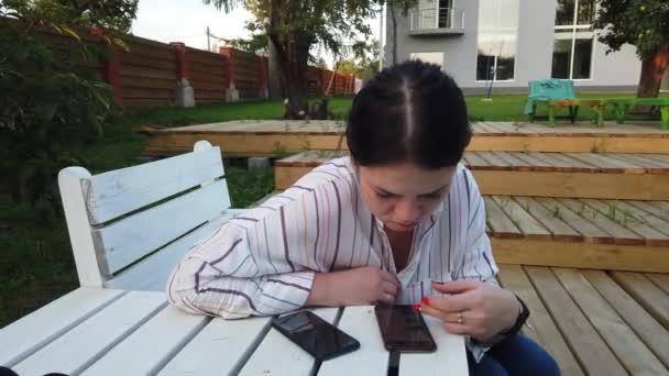 女性の携帯電話の使用と庭の家のベンチに座って — ストック動画
