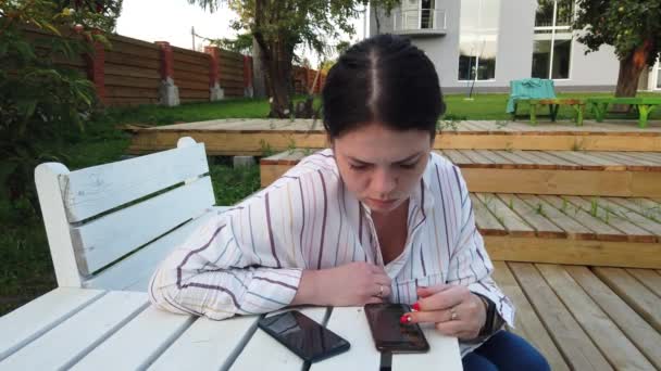 女性の携帯電話の使用と庭の家のベンチに座って — ストック動画