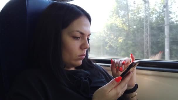 美丽的年轻女孩坐在火车的车厢里 用智能手机 发短信给朋友 看着窗户 — 图库视频影像