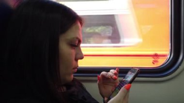 Trenvagongüzel genç kız koltuklar ve akıllı telefon kullanmak, arkadaşlarınıza mesaj mesajlaşma ve pencereden bakarak