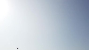 Savaş alanında askeri helikopter yavaş çekimde geçerek havai uçar. Mavi gökyüzü ve bulutlar. 4k Uhd yavaş çekim ham video görüntüleri 60 fps