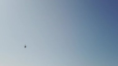 Savaş alanında askeri helikopter yavaş çekimde geçerek havai uçar. Mavi gökyüzü ve bulutlar. 4k Uhd yavaş çekim ham video görüntüleri 60 fps
