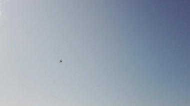 Savaş alanında askeri helikopter yavaş çekimde geçerek havai uçar. Mavi gökyüzü ve bulutlar. 4k Uhd yavaş çekim ham video görüntüleri 60 fps