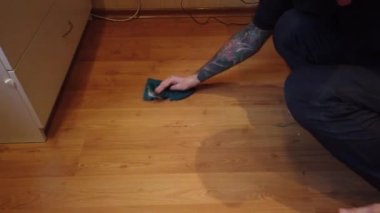 Genç adam evde yerleri yıkıyor. Bir adamın ahşap zemindeki kiri özel bir bezle temizlerken..