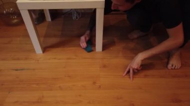 Genç adam evde yerleri yıkıyor. Bir adamın ahşap zemindeki kiri özel bir bezle temizlerken..