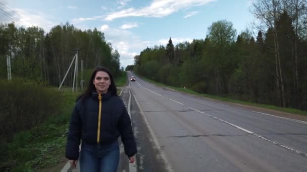 女の子は空の道を歩き 車のヒッチハイクをしようとします — ストック動画