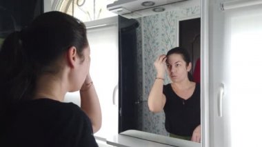 Güzel esmer kadın banyoda aynanın önünde makyaj yapıyor.