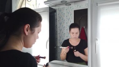 Güzel esmer kadın banyoda aynanın önünde makyaj yapıyor.