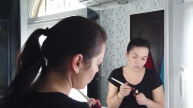 Güzel esmer kadın banyoda aynanın önünde makyaj yapıyor.