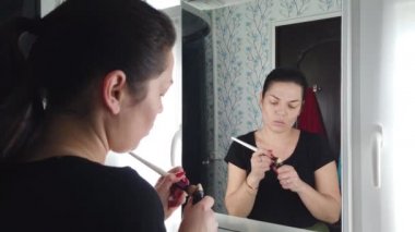 Güzel esmer kadın banyoda aynanın önünde makyaj yapıyor.