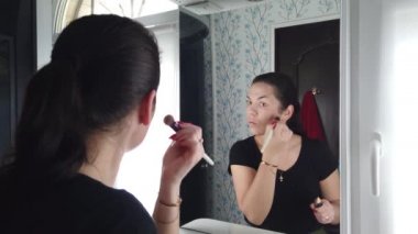 Güzel esmer kadın banyoda aynanın önünde makyaj yapıyor.