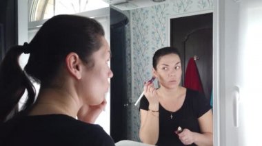 Güzel esmer kadın banyoda aynanın önünde makyaj yapıyor.