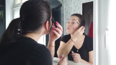 Güzel esmer kadın banyoda aynanın önünde makyaj yapıyor.