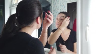 Güzel esmer kadın banyoda aynanın önünde makyaj yapıyor.