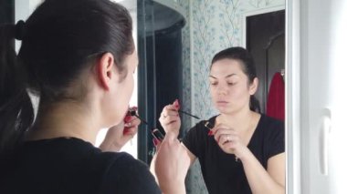 Güzel esmer kadın banyoda aynanın önünde makyaj yapıyor.