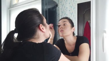 Güzel esmer kadın banyoda aynanın önünde makyaj yapıyor.