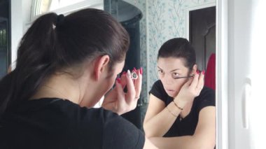 Güzel esmer kadın banyoda aynanın önünde makyaj yapıyor.