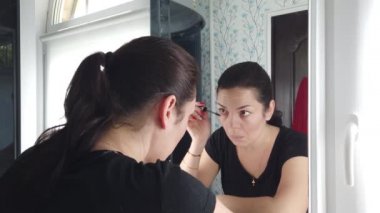 Güzel esmer kadın banyoda aynanın önünde makyaj yapıyor.