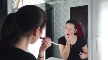 Güzel esmer kadın banyoda aynanın önünde makyaj yapıyor.