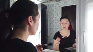 Güzel esmer kadın banyoda aynanın önünde makyaj yapıyor.