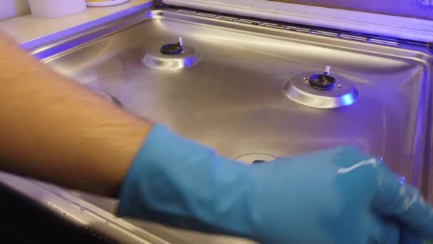 Mężczyzna w niebieskich rękawiczkach poleruje kuchenkę gazową w kuchni. — Wideo stockowe