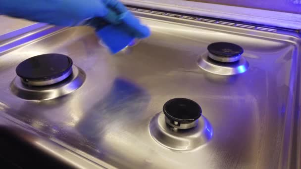A man in blue gloves polishes his gas stove in the kitchen — Stock Video