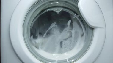 Beyaz çamaşır makinesi kirli renkli giysileri yıkar. Çamaşır makinesinde çamaşır yıkamak. Dönen davul çamaşır makinesinin videosunu kapat.