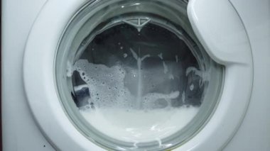 Beyaz çamaşır makinesi kirli renkli giysileri yıkar. Çamaşır makinesinde çamaşır yıkamak. Dönen davul çamaşır makinesinin videosunu kapat.