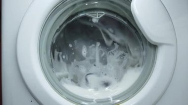 Beyaz çamaşır makinesi kirli renkli giysileri yıkar. Çamaşır makinesinde çamaşır yıkamak. Dönen davul çamaşır makinesinin videosunu kapat.