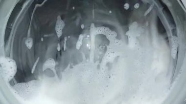 Beyaz çamaşır makinesi kirli renkli giysileri yıkar. Çamaşır makinesinde çamaşır yıkamak. Dönen davul çamaşır makinesinin videosunu kapat.