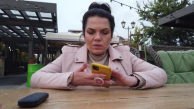 Kız, restorandaki verandada siparişi bekliyor. Sohbet ediyor, e-sigara içiyor.