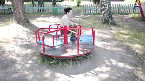 Menina adulta gira no carrossel do parque infantil — Vídeo de Stock