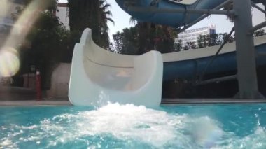 Aquapark 'ta su kaydırağına binen ve yüzme havuzunda suya düşen genç bir kızın yavaş çekim videosu.
