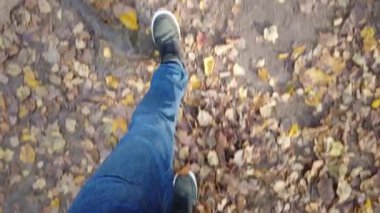 Spor ayakkabılı erkek ayakları yere doğru ilerliyor. Düşen sarı yapraklarla kaplı. Sonbahar başlangıcı konsepti, yakın plan, parkta ilerlemek..