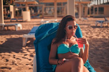 Kokteyl ve dinleme müzik telefonunu sahilde içme esmer