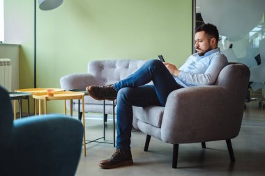 Ciddi bir adam sandalyede oturuyor ve cep telefonuna bakıyor.