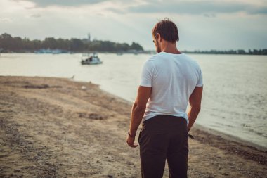 Üzgün uygun adam sahilde duran ve umutsuzluk içinde aşağı bakıyor