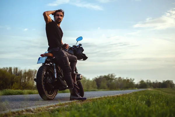 Macho man sitting on his bike in the middle of the road and holding his hair