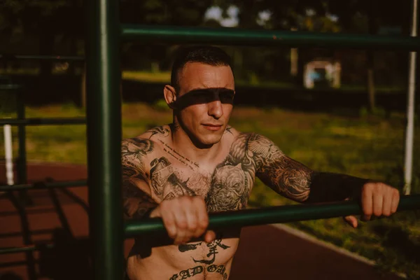 Duro Hombre Tatuado Apoyado Barra Entrenamiento Afuera Mirando Lejos — Foto de Stock